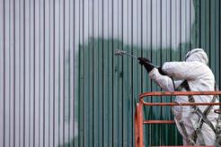 Un pintor profesional con equipo de protección total en una góndola. Pinta el revestimiento de un edificio de metal.