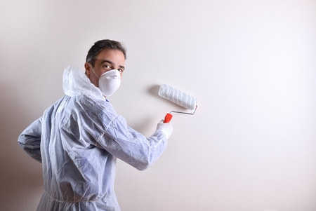 Maestro pintor de espalda sosteniendo un pergamino en su mano derecha. Lleva una máscara protectora y su cara está al revés.